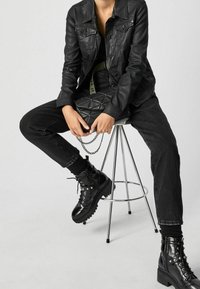 Schwarze Lederjacke über einem schwarzen Oberteil, kombiniert mit schwarzen Jeans und hochsohlen Schnürstiefeln. Eine gesteppte schwarze Handtasche mit einer Kettenriemen.