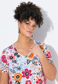 Top de cuello en V con estampado floral que presenta un fondo blanco con flores rosas, naranjas y amarillas. Mangas cortas y tejido suave con un ajuste relajado.