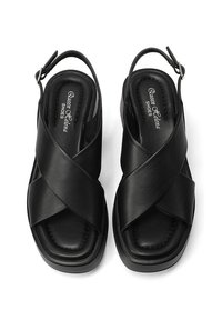 Sandali slingback in pelle nera con design a strap incrociati, soletta imbottita, punta quadrata e una texture sottile. Chiusura con fibbia regolabile.