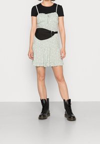 Ljusgrön blommig klänning med volangkant, bärs över en svart t-shirt; accessoriserad med en svart midjeväska och svarta snörkängor.