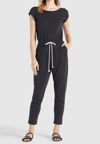 Zwarte jumpsuit van zachte stof, met korte mouwen, een taille met trekkoord en kwastjes, en taps toelopende benen.