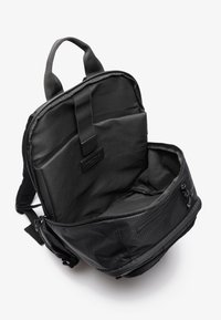 Sac à dos noir avec un intérieur rembourré, des bretelles ajustables, une poignée supérieure, un compartiment zippé externe et une finition en tissu lisse et texturé.