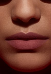 Matte, mauve lipstick on smooth lips, framed by a subtly glowing skin tone, creating a soft contrast against a blurred dark background.