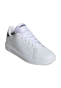 Zapatilla deportiva blanca con parte superior de piel lisa, suela plana, punta redondeada y detalles en negro en el talón. Presenta franjas laterales perforadas y cordones.