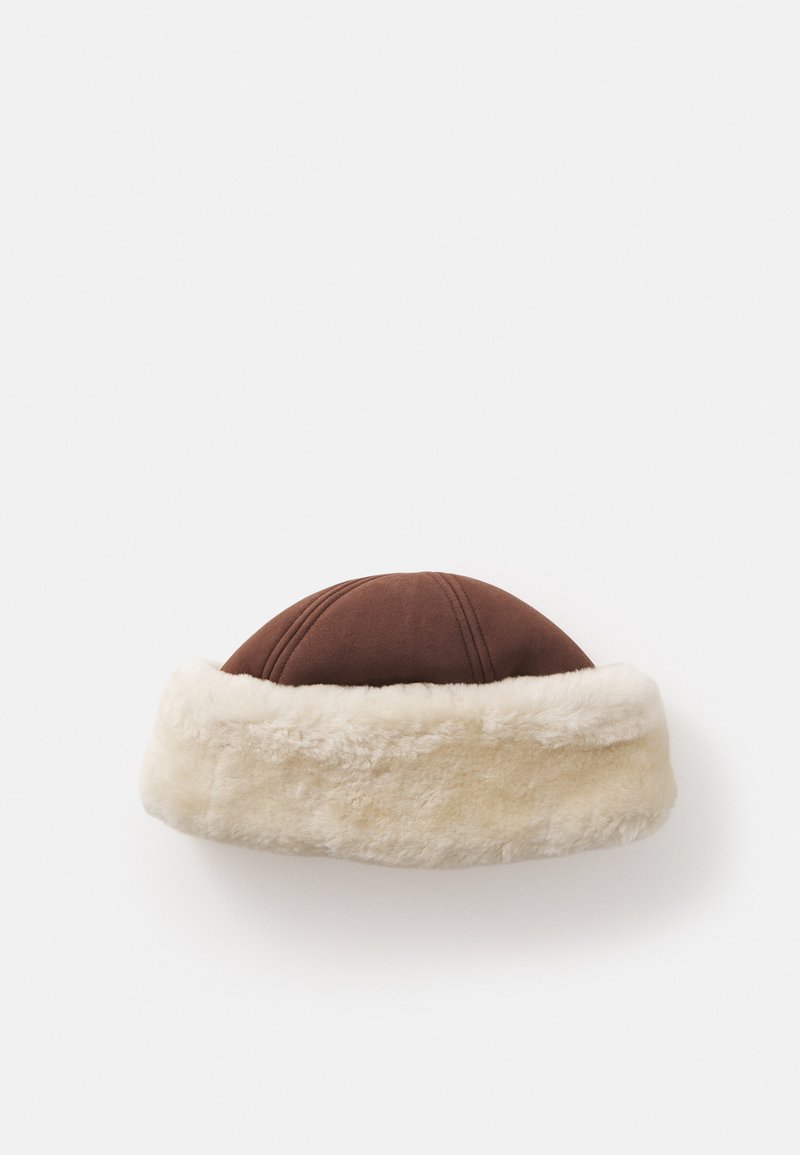 Chapeau marron avec un sommet rond et un large bandeau en fausse fourrure crème, présentant des coutures visibles sur la partie supérieure. Texture douce et design chaleureux.