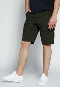 Mørkegrønne cargoshorts med foran og sidelommer, lavet af letvægtsstof, parret med hvide sneakers med et klassisk design.