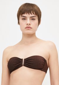Brūns, mirdzošs bezplecu bikini tops ar savilkta auduma detaļām un zelta akcentu centrā. Gluda tekstūra, pielāgota dizaina, bez siksnām.
