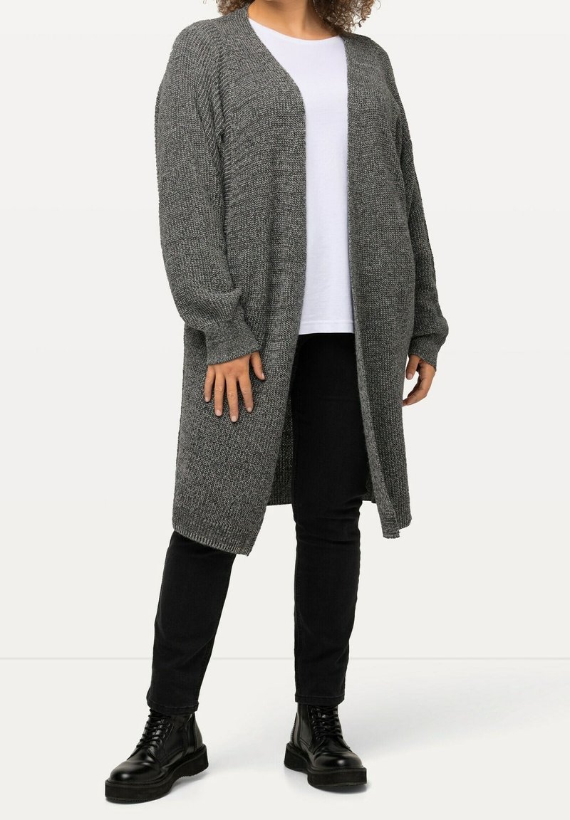 Long, open-front cardigan in a textured gray knit, with dropped shoulders and ribbed cuffs, worn over a white shirt and black pants.