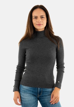Pull col roulé côtelé gris foncé à manches longues, avec des accents de boutons aux poignets, associé à un jean en denim bleu clair.