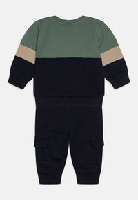 To-delt antrekk med grønn, beige og marineblå fargeblokkdesign. Laget av mykt stoff med ribbede mansjetter og cargo-lommer på buksene.
