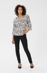 Blouse à motif floral noir et blanc avec des manches trois-quarts, associée à un pantalon skinny noir et des chaussures noires à talons pointus.