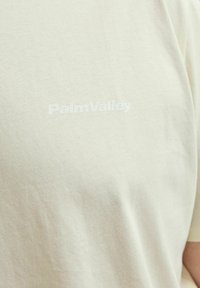 Svijetlosmeđa majica od mekanog pamuka, s blagom teksturom i utisnutim logotipom "PalmValley" na prednjoj strani u bijeloj boji.