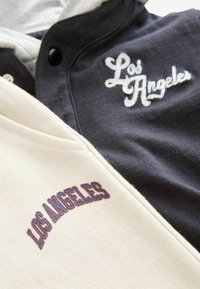 Sweatshirt à capuche beige clair et gris avec "Los Angeles" brodé dans des couleurs contrastées. Comprend des boutons et un design bicolore.