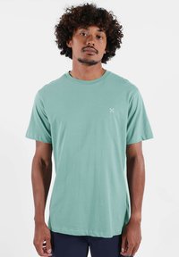 T-shirt à manches courtes vert menthe en tissu doux, avec un col rond et un petit logo sur le côté gauche de la poitrine.