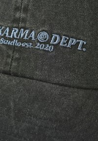 Mörkgrått tyg med ljusblå broderad text som säger "FARMA@DEPT. Estd. 2020" på en texturerad yta.