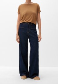 Brun kortærmet top parret med højtaljede, brede mørkeblå jeans med kontrastsyninger og knaplukning.