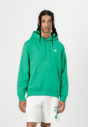 Felpa verde con cappuccio in cotone, dotata di tasca anteriore e piccolo logo Nike bianco sul petto. Indossata con pantaloni corti bianchi.