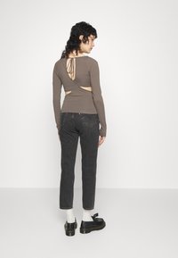 Top castanho de mangas compridas com um design de costas recortadas e detalhe de laço, combinado com jeans cigarrete pretos e sapatos pretos. Textura de tecido suave.