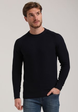 Navy blue textured sweater with a crew neckline and long sleeves, featuring ribbed cuffs and hem. Worn with light blue jeans.