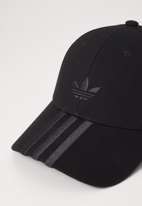 Casquette noire avec une visière incurvée, ornée d'un logo brodé ton sur ton et de trois rayures texturées à l'avant. Fabriquée en tissu lisse.