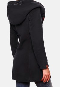 Cappotto di pile nero con un grande cappuccio, con un logo ricamato sul retro e dettagli in pelle sui polsini.