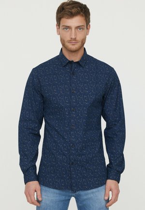Chemise à manches longues bleu marine avec un motif floral, fermeture à boutons et col. Fabriquée dans un tissu texturé, associée à un jean bleu clair.