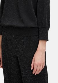 Vêtement noir texturé avec des éclats métalliques, présentant une coupe décontractée, des poignets élastiques et une taille lisse ; adapté pour une tenue décontractée.