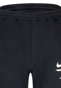 Ingrandimento di pantaloni da tuta neri con elastico in vita e logo Nike parzialmente visibile in bianco sulla gamba destra.