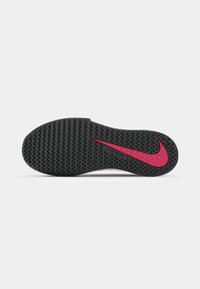 Svart gummisåle med teksturert mønster, med en fremtredende rosa Nike swoosh-logo og et strømlinjeformet design.