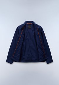 Μπλε ναυτικού ανοιχτόχρωμο μπουφάν με μακριά μανίκια, πορτοκαλί εσωτερικές ραφές και ένα μικρό πλαίσιο στο αριστερό μανίκι, απλωμένο σε ανοιχτόχρωμη επιφάνεια.