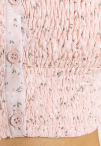 Gros plan d'un tissu rose avec un petit motif floral, texture élastique froncée et trois boutons roses sur la couture latérale d'un vêtement.