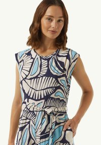 Sukienka z krótkim rękawem w niebiesko-białe wzory liści na ciemnym tle, z wiązanym pasem i bocznymi kieszeniami. Miękka tekstura materiału.