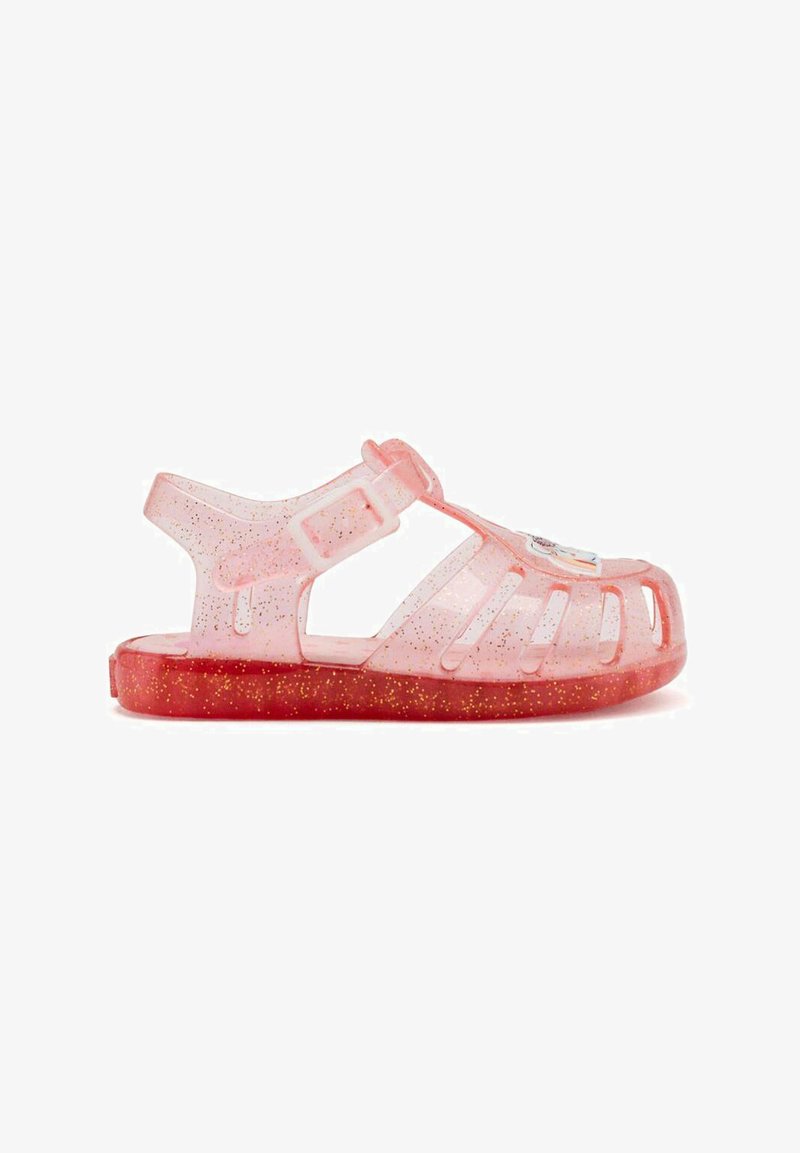 Sandal de gelatina translúcida rosa con suela roja brillante. Presenta recortes, correa ajustable y un acento colorido en la punta.