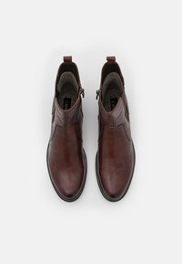 Bottines en cuir marron à texture lisse, forme angulaire, fermetures éclair latérales et semelle contrastante. Logo de la marque visible à l'intérieur.