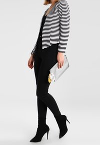 Randig kavaj i svart och vitt, åtsittande svart topp, svarta skinny jeans och svarta spetsiga ankla stövlar. Silverfärgad kuvertväska med dekorativa detaljer.