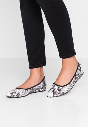 Baleriny z czarno-białym wzorem w skórę węża, zaokrąglonym noskiem i kontrastową czarną lamówką; na osobie noszącej czarne spodnie.