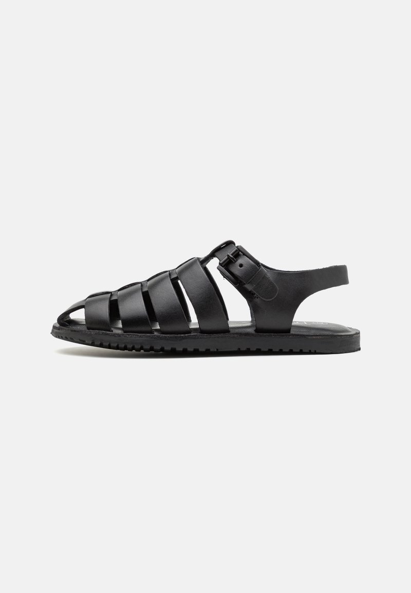 Zwarte leren sandalen met een strapdesign, een verstelbare gesp en een platte rubberen zool met een gestructureerd profiel.