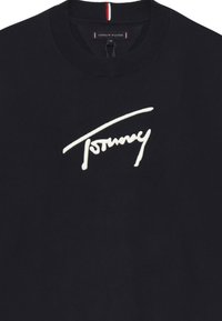 Maglione nero girocollo con la firma "Tommy" ricamata in bianco sul petto e un'etichetta Tommy Hilfiger all'interno del colletto.