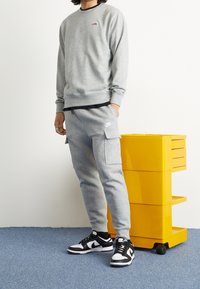 Šedá mikina s kulatým výstřihem a malým logem, doplněná o šedé cargo tepláky s kapsami. Černo-bílé sneakers dokončují vzhled.