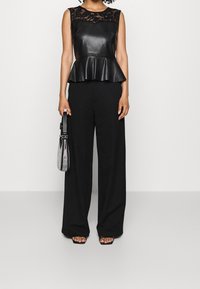 Černý peplum top s krajkovým výstřihem, doplněný širokými černými kalhotami. Doplňky zahrnují malou stříbrnou síťovanou kabelku.