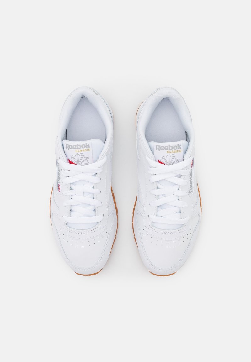 Baskets en cuir blanc avec des perforations, lacets blancs plats et semelle en caoutchouc gomme. Présente le logo Reebok sur la languette et les côtés.