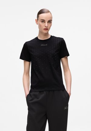 T-shirt in cotone nero con un motivo di decorazione a pois sulla parte anteriore e un logo sottile, abbinato a pantaloni neri a vestibilità rilassata.