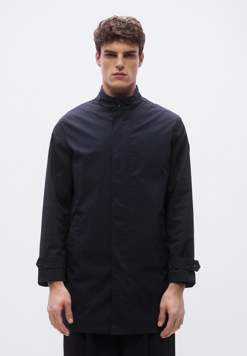 Black, long-sleeve jacket with a stand collar. Made from a smooth, water-resistant material. Features buttoned cuffs and a minimalistic design.
