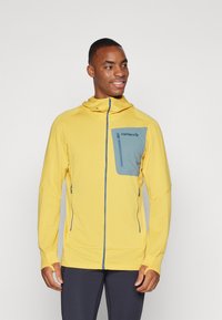 Yellow zip-up hoodie with a blue chest pocket, long sleeves, and thumb holes. Made of textured material, features a hood and zippered pockets.