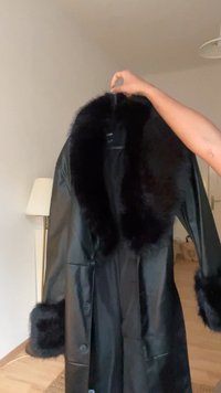 Fekete műbőr kabát műszőrme gallérral és mandzsettákkal. Gombokkal az elején és oldalzsebekkel rendelkezik. Simán textúrázott és hosszú ujjú.