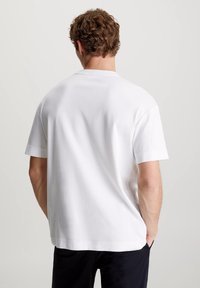 White cotton short-sleeve t-shirt with a relaxed fit. Features a rounded neckline and smooth texture, shown from the back.