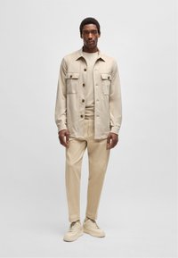 Beige overhemd met knopen en twee borstzakken, gecombineerd met een bijpassend T-shirt met ronde hals en tailored broeken. Gestructureerde stof en schoenen in een neutrale tint.