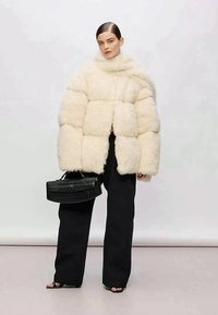 Casaco puffer de pelo falso beige claro com um colarinho alto e forma boxy, combinado com calças largas pretas e uma bolsa preta texturizada.