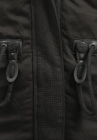 Zwarte jas met een gladde stof, zichtbare stiksels en ronde sluitingen met bijpassende koorden. Verstevigd met leren hardwaredetails.