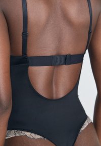 Μαύρο μαγιό με λεπτές straps, που διαθέτει χαμηλή κοπή στην πλάτη και λουλούδια από δαντέλα στη βάση. Λείος υφασμάτινος χαρακτήρας, ραφή χωρίς ραφές.